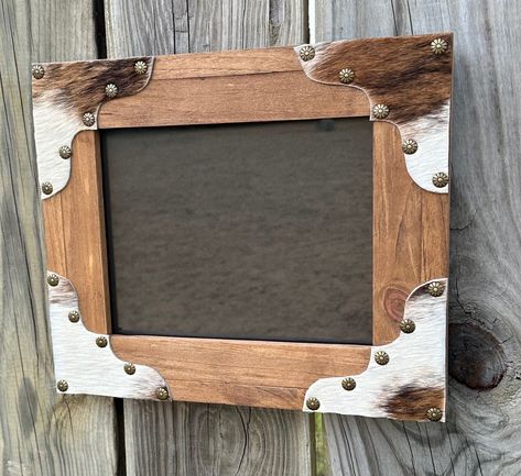 I hand craft these frames from pine wood. They are stained in Minwax Early American stain. The corners feature red/white with shades of brown cowhide scallops with antique brass daisy nailhead trim. The hide may differ slightly from the photo, but will have the same colors and be used from the same hide as pictured . These hold an 8x10 picture, overall dimensions are 12x14. They have a hanger for horizontal hanging but can sit on a tabletop or hang vertically by the frame. Customization is available as well as bulk orders, shown in the last picture. Cowhide Picture Frame, Cowhide Projects, Cowhide Crafts, Western Mirror, Buckle Display, Hunting Crafts, Early American Stain, Cowhide Decor, Hats Ideas