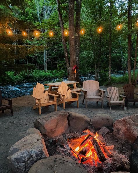 Fire pit along the waters edge of a rushing river with string lights above to complete the comfortable vibe of the natural surroundings