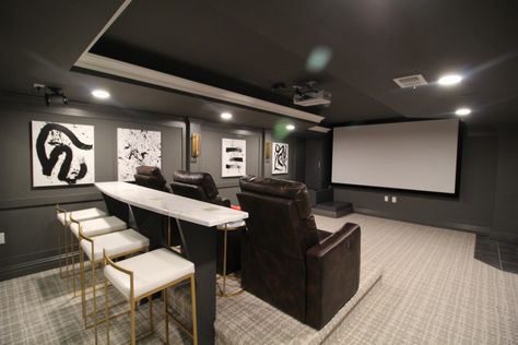 Elegant and enveloping are the two adjectives that best describe this theater. The dark charcoal walls accented by custom trim and a tray ceiling set the movie mood, while high hats and sconces provide ample lighting when desired. Three leather recliners on a platform enable viewers to watch a movie on the big screen in comfort. Basement Tv Area, Dark Basement Ideas, Install Crown Molding, Easy Basement Ceiling, Basement Movie Room, Basement Paint Colors, Dark Basement, Charcoal Walls, Black Page