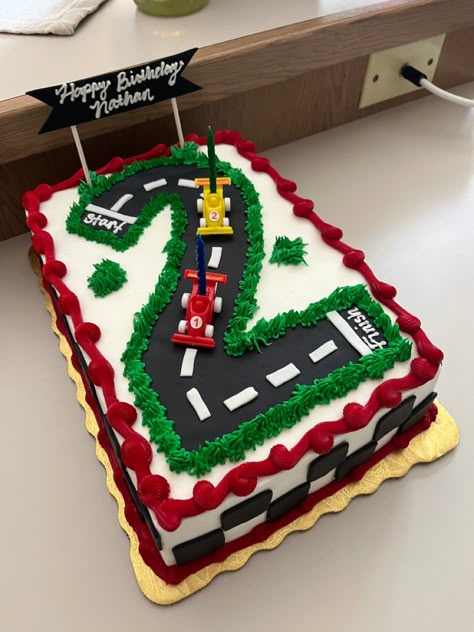 Sheet cake with a large number 2 designed like a race track with two race cars. Checkered border made of fondant, green grass made of buttercream.  Also has a banner that reads Happy Birthday, Nathan. 2 Race Car Cake, Lightening Mcqueen Sheet Cake, Two Fast Race Car Birthday Cake, Two Fast Racing Birthday Party, Racetrack Birthday Cake, Two Fast Sheet Cake, Race Car 2nd Birthday Cake, Smash Cake Race Car Theme, Blaze Birthday Party Ideas Cakes