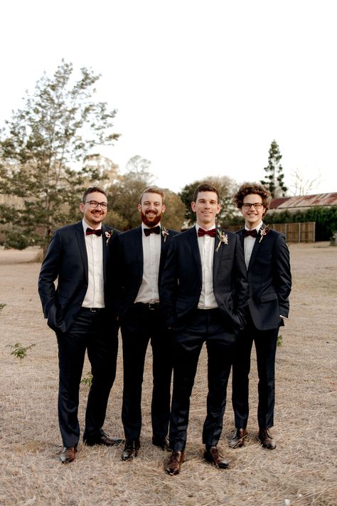 How lovely is it to see all these groomsmen in their classic suits with a burgundy bow tie. So simple with a small pop of colour. Black Suit Burgundy Tie Wedding, Christmas Groomsmen Attire, Black Suit Burgundy Tie, Christmas Wedding Groomsmen, Christmas Wedding Suits, Groomsman Ideas, Black Groomsmen Suits, Navy Groomsmen, Groom Suit Black