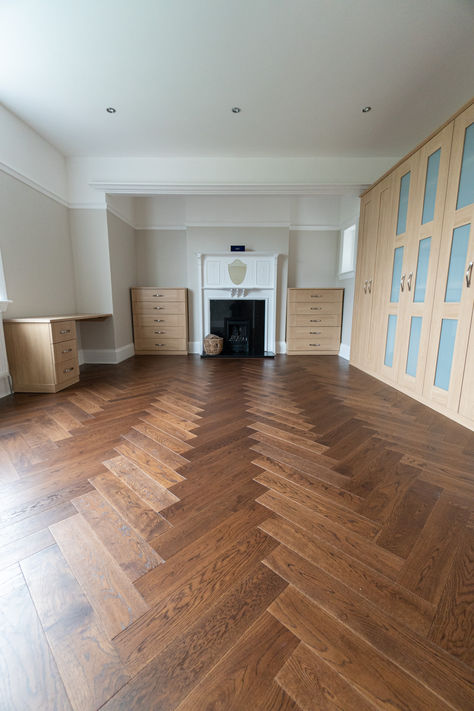 Spacious room featuring dark oak herringbone wood flooring, built-in light oak wardrobes, and a decorative white fireplace, creating a sophisticated and elegant atmosphere. Flooring Ideas Dark, Luxury Flooring Ideas, Wood Bedroom Floor, Interior Flooring Ideas, Flooring Ideas Bedroom, Herringbone Pattern Wood, Wood Flooring Design, Wood Floor Inspiration, Home Interior Design Luxury