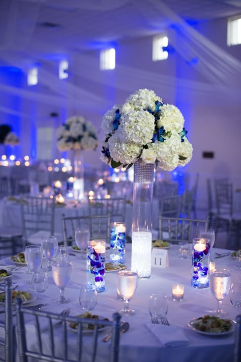 White and Silver Reception Decor with Blue Uplighting Wedding Decorations Blue, Silver Wedding Centerpieces, Blue Uplighting, Royal Blue Wedding Theme, Silver Wedding Theme, Blue Silver Weddings, Royal Blue Quinceanera, Blue Wedding Receptions, Uplighting Wedding