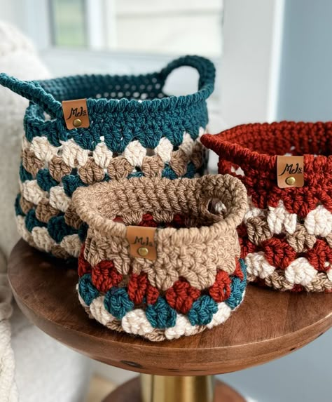 Three crocheted Granny Stitch Baskets in varying sizes and colors sit on a wooden surface. Each basket has a label reading "Mo's" and showcases a mix of teal, beige, and rust hues. Easy Crocheted Christmas Gifts, Crochet Organization Ideas, Crochet Projects With Cotton Yarn, Granny Square Gifts, Unique Crochet Ideas, Crochet House Decor, Crochet Caddy, Easy Crochet Gifts, Easy Christmas Crochet