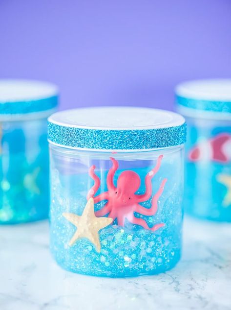 DIY Glitter Ocean Slime Jars – this aquarium inspired craft is a great summer boredom buster idea for kids! This easy slime recipe will show you how to make glitter slime with ocean toys to store in plastic containers. Great for saving as a summer activity or party favor for an Under the Sea party! Ocean Slime, Science Party Favors, Glitter Slime Recipe, Slime Containers, Under The Sea Crafts, Crafts With Glass Jars, Snow Globe Crafts, Ocean Birthday Party, Summer Boredom