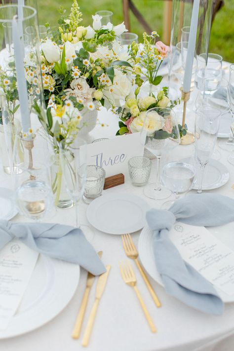 Newport, RI summer garden-style wedding. Gold flatware, light blue candlesticks and chamomille arrangements Dusty Blue Wedding Centrepiece, Pale Blue Wedding Centerpieces, White Tablecloth Blue Napkins Wedding, Light Blue Tablescape, Spring Wedding Round Table Settings, Light Blue Wedding Table Decor, Light Blue Wedding Table, Blue Napkins Wedding, Coastal Tablescapes