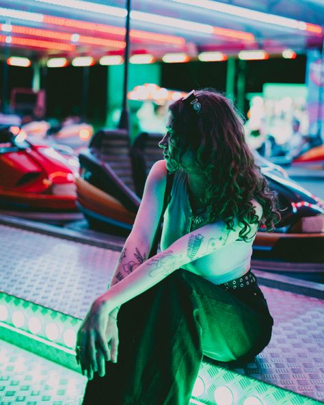 A girl with long curly hair is at a fair all alone. She is sitting by the bumper cars while in green lights. Fun Fair Photoshoot, Euphoria Lighting, Euphoria Carnival, Carnival Shoot, Curly Hair Brunette, Euphoria Vibe, Carnival Photoshoot, Carnival Photo Shoots, Park Editorial