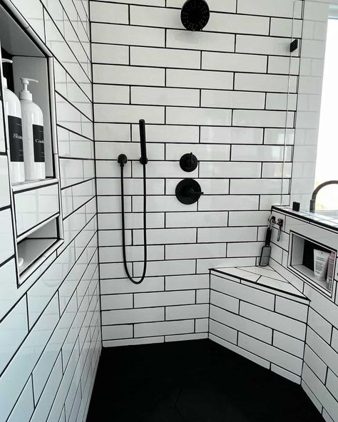 Shower bench ideas are displayed in this bathroom with a corner bench and a built-in niche. White subway tile with black grout displays a black faucet and a second niche on the opposite wall. Black flooring contrasts with the white space. Subway Tile Shower With Niche, Subway Tile With Black Grout, Shower Bench Ideas, Black Bathroom Floor Tiles, Tile With Black Grout, White Tiles Black Grout, Shower Niche Ideas, Pebble Tile Shower, Black Bathroom Floor