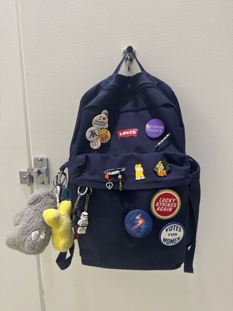 Navy blue backpack with various pins and keychains Levis Backpack, Backpack With Pins Aesthetic, School Bag Keychain, Keychains On Backpack, Backpack Customize Ideas, Customized Backpack, Backpack Keychain, Backpack Accessories Keychain, Decorated Backpack