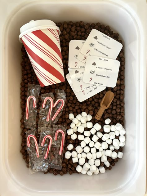 Hot Cocoa sensory kit This sensory bin includes:   * 6 cups of Cocoa puffs * 1 cup of marshmallows  * 1 mini wooden spoon * 6 mini candy canes * 1 coffee cup with lid * 6 laminated playing cards *NOTE*  This activity set does NOT include the bin, you can purchase cheap bins from the store to fit your preference. The bins I use are from the IKEA for $4.99.  *Just for thought* Easier: This sensory bin can be for the really early toddler who doesn't know his/her numbers yet. Let them explore and pl Sensory Bins Kinetic Sand, Sensory Bin For Three Year Old, Sensory Bin Gift Ideas, Make Your Own Sensory Bin, Marshmallow Sensory Bin, Birthday Party Sensory Play, How To Store Sensory Bin Items, Sensory Bins Christmas, Preschool Christmas Sensory Bin