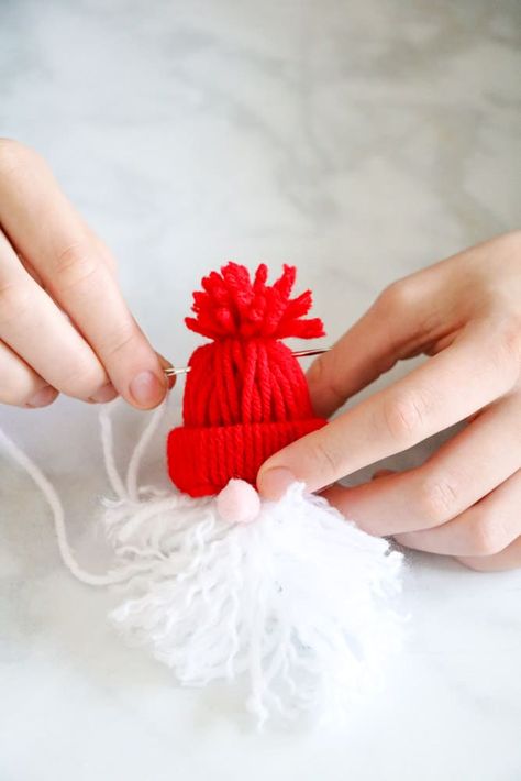 Step by step instructions on how to make mini yarn winter hat Santa garland. This fun Santa beanie DIY project is easy to create and add to your Christmas decorations. Directions include a video tutorial. Add this cute do it yourself red and white Santa and wooden bead garland to your kitchen hutch, furniture, fireplace mantel, or any room. Santa Pom Pom Ornament, Yarn Santa Hat Ornament, Yarn Hat Garland, Hat Garland Diy, Yarn Santa, Santa Garland, Christmas Yarn Crafts, Hat Garland, Beanie Diy