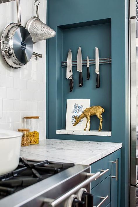 A magnetic knife rack and marble shelf are fixed in a rectangular niche positioned near a stainless steel oven range located against white subway backsplash tiles, beneath a wall mount pot rack, and beside blue cabinets adorned with long satin nickel pulls and a carrera marble countertop. Kitchen Niches, Kitchen Niche, Magnetic Knife Rack, Kitchen Innovation, Marble Shelf, Pot Racks, Blue Kitchen Cabinets, Knife Rack, Wall Niche