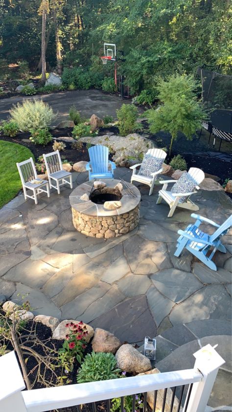 Designed by Chris Kennedy of Kennedy's Country Gardens, built winter of 2019. Steel ring inside, fieldstone wall, blue stone cap, fieldstone pokes through cap for style, irregular bluestone patio. Used stones from property and re-graded to flatten space to make usable.  We use natural flat stones to creat stairs to lower level and access to basketball court and trampoline.  Used Trees and shrubs to hide trampoline.  See other pic to see how we highlight the space and trees with nightlighting. Blue Stone Patio With Fire Pit, Flagstone And Paver Patio, Tumbled Bluestone Patio, Bluestone Flagstone Patio, Fieldstone Patio Ideas, Field Stone Patio, Stone Terrace Patio, Irregular Stone Patio, Irregular Bluestone Patio