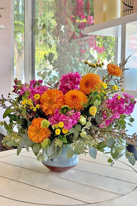 Be captivated by the unexpected beauty of our Dahlia Surprise arrangement. A stunning collection of vibrant orange dahlias, bright pink stock, delicate green hellebores, and sunny yellow tanzines surrounded with seeded eucalyptus leaves is artfully composed within a sophisticated dusty blue ceramic vase. This exquisite floral masterpiece creates a striking contrast of colors and textures, making it a truly unforgettable gift for any occasion. Featured Flowers: Dahlias, Stock, Hellebores, and TanzineRecommended for: Birthday, Get Well Soon, Friendship, Congratulations, and HousewarmingIncludes: Free message card Delivery: Enjoy same-day flower delivery anywhere in Los Angeles and Orange County. Unique Pink Flowers, Orange Alstroemeria Bouquet, 2025 Floral Trends, Dahlia Floral Arrangements, Eucalyptus Floral Arrangements, Bright Flower Arrangements, Whimsical Flower Arrangements, Whimsical Floral Arrangements, Flower Table Centerpieces