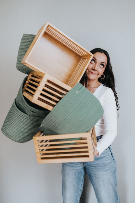 A woman with dark hair wearing a white long-sleeve shirt and blue jeans is holding a stack of balancing green fabric baskets and wooden crates while look up and to the right. Staging Branding Photos, Organizer Branding Shoot, Professional Home Organizer, Professional Organizer Photoshoot, Personal Organizer Ideas, Linen Photoshoot, Professional Organizer Business, Branding Headshots, Co Branding