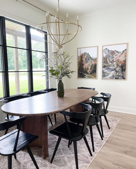 Stained wood oval dining table is lit by a gold chandelier in this dining room with black frame windows. Black wishbone chairs are seated around the table on a white and light purple rug. Dining Table Decoration Ideas, White Oval Dining Table, Dark Wood Dining Room, Wood Oval Dining Table, Oval Wood Dining Table, Eagle Landing, Dark Wood Dining Table, Oval Dining Room Table, Living Room Decoration Ideas