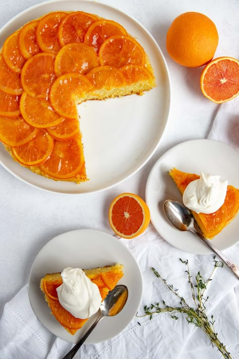 Orange upside-down cake on a plate surrounded by whole and cut oranges and two slices of cake on dessert plates Orange Cake Upside Down, Orange Torte Cake, Orange Shaped Cake, Orange Upside Down Cake Recipes, Tangerine Upside Down Cake, Upside Down Orange Cake, Citrus Upside Down Cake, Orange Slice Cake, Orange Upside Down Cake