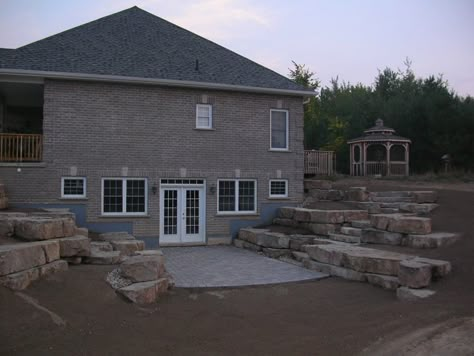 Walkout basement with limestone tiered retaining walls, this is similar to how the west side of our home will look like when removing the hillside and opening it up to a walkout with a deck above. Walkout Basement Patio, Basement Window Replacement, Rock Steps, Basement Doors, Basement Entrance, Concrete Retaining Walls, Basement Layout, Stone Retaining Wall, Landscaping Retaining Walls