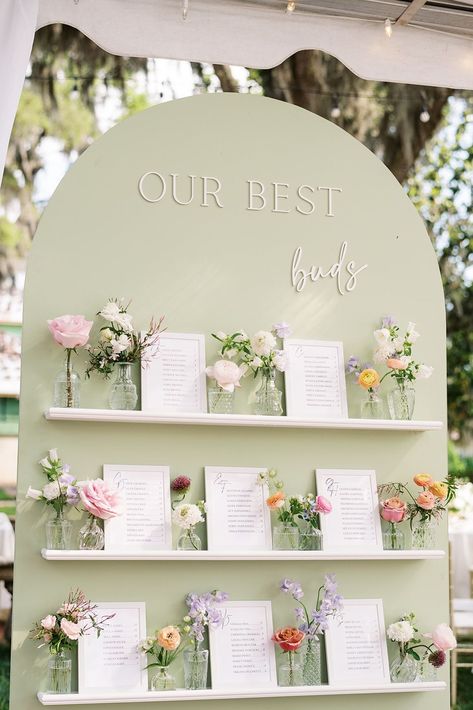 Romantic wedding seating chart display with a soft green backdrop, pastel floral arrangements, and framed guest lists for a modern yet timeless touch. Perfect for outdoor, garden, or elegant wedding designs, this creative idea combines stylish functionality and stunning decor. Garden Wedding Diy Decorations, Wedding Day Seating Chart, Botanical Seating Chart, Floral Table Seating Chart, Flower Table Seating Chart, Wedding Seating Chart Sign Ideas, Flowers Theme Wedding, Seat Wedding Chart, Best Buds Wedding Seating Chart