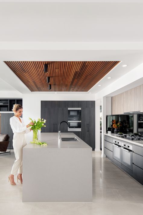 A dropped ceiling and timber panel feature above a grand island bench is the perfect addition to any luxury kitchen. Visit this stunning space at our Bayside 39 MKII home, on display at Newport. Kitchen Timber Ceiling, Feature Island Bench, Timber Ceiling Kitchen, Ceiling Fan Above Kitchen Island, Drop Down Ceiling Over Kitchen Island, Kitchen Island Ceiling Ideas, Ceiling Above Kitchen Island, Drop Ceiling Kitchen, Kitchen Island Ceiling