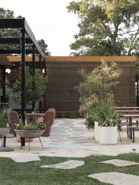 The restaurant courtyard has outdoor furniture by Katie Lockhart Studio: cast terracotta-colored concrete furniture, and tables and benches from Street Furniture with bases that Katie powder-coated in Dulux Denim Blue. Jared designed a path of irregular stone slabs; at the base of the pavilion building, the pavers are set close together and after they reach the parkland grass, the pavers drift apart. #gardenista Restaurant Courtyard, Katie Lockhart, Colored Concrete, Outdoor Patio Ideas, Front Courtyard, Outdoor Living Design, Backyard Remodel, Concrete Furniture, Backyard Pergola