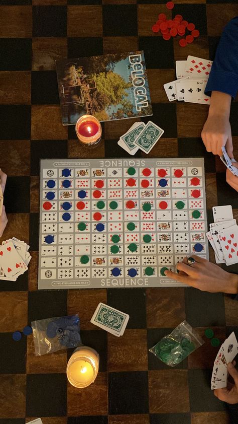 top-down overhead photo of sequence (the board game) splayed across a black and brown wooden coffee table as three people are playing the game, two candles are lit on the table Cabin Aesthetic With Friends, Checkers Game Aesthetic, Cabin Weekend Activities, Family Board Games Aesthetic, 30th Birthday Cabin Weekend, Cozy Cabin Vibes, Cabin Party Aesthetic, Family Game Night Aesthetic, Board Game Night Aesthetic