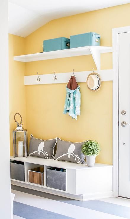 Yellow and blue mudroom features walls painted bright yellow lined with a shelf lined with blue bins and a row of hooks over a built-in bench filled with galvanized steel bins and gray pillows alongside a gray striped floor. Bathroom Blue Grey, Blue Mudroom, Striped Walls Vertical, Gray Striped Walls, Grey Striped Wallpaper, Yellow Hallway, Grey Striped Walls, Transitional Laundry Room, Yellow Accent Walls