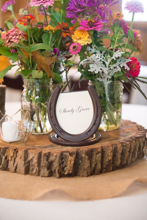 Wildflower centerpieces. The bride and her family planted wildflowers in the spring and used the brilliant blooms in stunning centerpieces. Assembled in simple mason jars placed on homemade wooden stands, the flowers added such a splash of color. Centerpieces were enhanced with tea lights in small glass votives and set on burlap table runners. Table markers were placed inside horseshoe picture frames, fitting with the barn venue. Horseshoe Centerpieces Ideas, Rustic Farm Wedding Centerpieces, Horseshoe Picture Frame, Horseshoe Centerpieces, Color Centerpieces, Wedding Guest Table Centerpieces, Picture Wedding Centerpieces, Jam Wedding Favors, Mason Jar Tea Lights