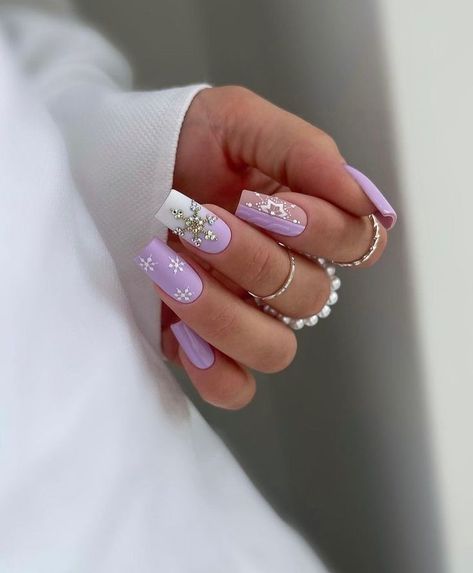 These nails feature a soft lavender base with delicate white snowflake designs and sparkling gem accents. The subtle winter theme is elegant and stylish, making it perfect for those looking to embrace the season with a touch of class. The combination of matte and shiny finishes adds depth and interest to this beautiful manicure. Purple Nail Art, Soft Lavender, Purple Nail, Soft Purple, White Snowflake, Snowflake Designs, Nail Wraps, Winter Theme, Manicure