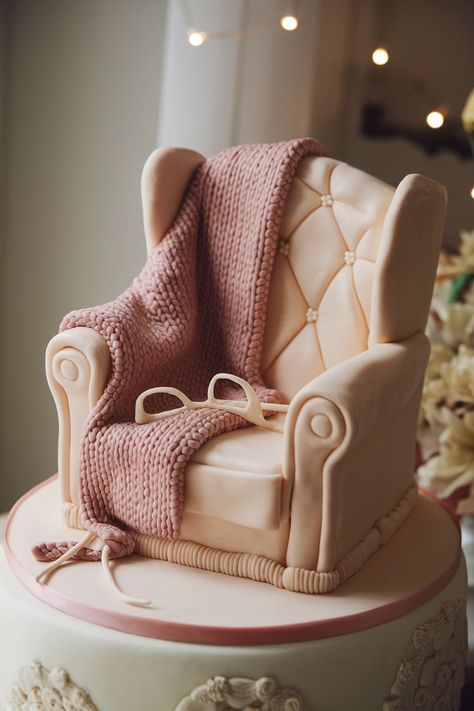 A cake shaped like a cozy armchair with a knitted blanket draped over it. A small knitting project and pair of glasses rest on the arm of the chair. The cake is in soft, warm colors. Avoid close-up shots of the cake decorations and show the entire cake wherever possible. Knitting Cake, Knitted Bunting, Cozy Armchair, Knitting Room, Small Knitting Projects, Silhouette Cake, Miniature Knitting, Knitting Club, Hat Cake