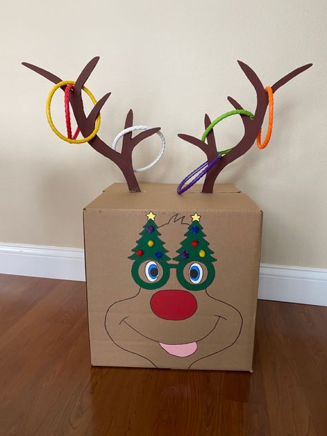 You’ll need a cardboard box, hot glue gun and paint.   I used the heavy card stock poster board at hobby lobby for the antlers so they would be more durable.   I cut a small slit in the top of the box and then hot glued the antlers into place to make them more sturdy.   I used the craft acrylic paints to add a silly face and then small Pom Pom balls for the tree decorations.   We are using the dive swim rings for the toss rings. Diy Christmas Party Games, Kindergarten Christmas Party, Preschool Christmas Party, Quiz Ideas, Christmas Tree Game, Christmas Party Games For Kids, Christmas Fair Ideas, Party Games For Kids, Christmas Party Activities