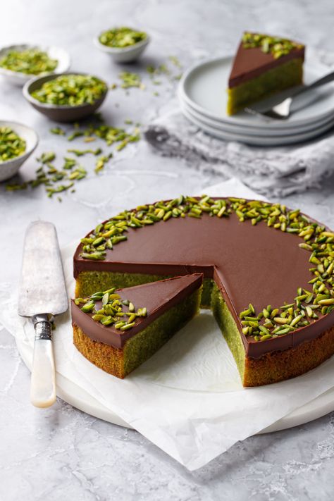 Flourless Pistachio Cake with Chocolate Ganache and topped with slivered pistachios, on a gray background with cake server, cut slice and more pistachios in the background. Pistachio Cake Recipe, Flourless Desserts, Chocolate Ganache Tart, Cake With Chocolate Ganache, Flourless Cake, Healthier Desserts, Pistachio Cake, Gluten Free Cake, Rib Recipes