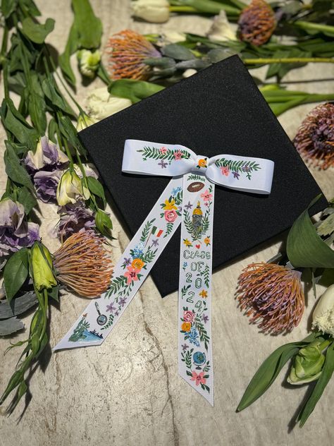 "completely customizable personalized hand painted bow to attach to graduation cap or wear in your hair. each bow is ~7\" wide and 11\" from top to bottom, attached to a small black elastic for easy looping onto the top of basic graduation caps. perfect gift for your favorite grad or the best way to stand out in a crowd! please choose base option of white or cream, or reach out for availability on custom colors. PLEASE NOTE, LISTING IS FOR BOW ONLY - HAT IS NOT INCLUDED" Christmas Graduation Cap, College Grad Hats Cap Decorations, Graduation Cap College Designs, Caps Graduation Decoration, Grad Cap Inspo College, Bachelor Graduation Cap, 3d Graduation Cap, Painted Grad Cap Ideas, Grad Cap High School