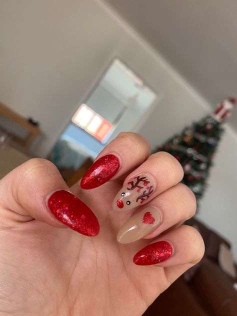 photo of acrylic nails in front of christmas tree. 3 nails are red with glitter and 2 are light brown. one has nail art of a small red love heart and the other has a reindeer with a red nose and red baubles hanging from his antlers. Rudolf Christmas Nails, Christmas Nails Red Reindeer, Cute Christmas Nails Reindeer, Christmas Nails Acrylic Reindeer, Rudolf Nails, Christmas Nails Rudolph Red Nose, Red Sparkly Nails, Reindeer Nails, Nail Art Red