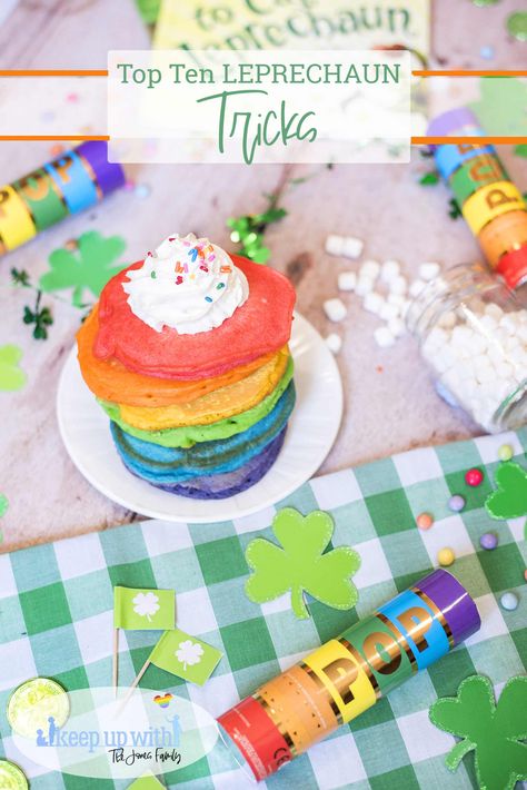 A colourful breakfast table set for St. patrick's day with green checkered tablecloth, a stack of bright rainbow coloured pancakes with whipped cream and sprinkles on top. There are glittery shamrock cut-outs and rainbow coloured candy. There are small shamrock food flags and rainbow confetti cannons with a jar of spilled marshmallows and How to Catch A Leprechaun book in the background. This post is about our top ten leprechaun tricks. Leprechaun Tattoos, Leprechaun Trap Project, Leprechaun Tricks, Leprechaun Gold, Easy Pranks, Rainbow Pancakes, Green Flags, Lucky Charms Cereal, The Leprechaun