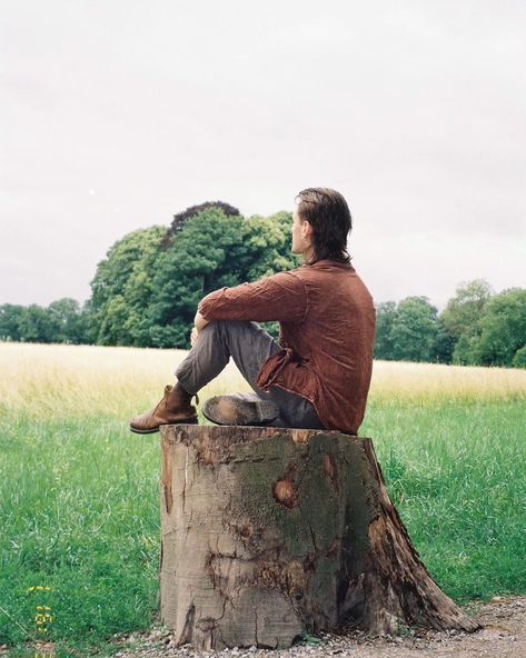 Person sitting on a log in a forest. They're wearing boots, green linen pants, and a brown blouse. They have a mullet and earrings. Person Sitting Down Looking Up, Sitting On Ground Reference Drawing, Sitting On A Log Reference, Person Sitting Looking Up, Person Sitting Against Wall Reference, Sitting Behind Reference, Person Sitting On Ledge, Person Sitting Back View, Person Sitting From Behind