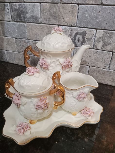 Beautifully made vintage 6 piece tea set made by Cracker Barrel. This set includes 6 Ivory porcelain pieces adorned with raised roses and 10k gold paint trim. It includes 1 tray, 1 teapot with lid, 1 Creamer and 1 sugar bowl with lid. Add to your collection today. Such a  beauty! Approximate size: TRAY 7 1/2" x 7 1/2" TEAPOT W/ LID 6 1/4 H" x 6" L CREAMER 3" H x 3 3/4 " L SUGAR BOWL 4" H x 4 1/2" L Please note these are items are vintage and may show some signs of wear. We believe this only adds Vintage Tea Pot, Kitchen Wear, China Tea Sets Vintage, Cottagecore Tea Set, Girls Tea Set, Pink Tea Set, Coquette Tea Set, Cute Tea Cups, Ornate Tea Set