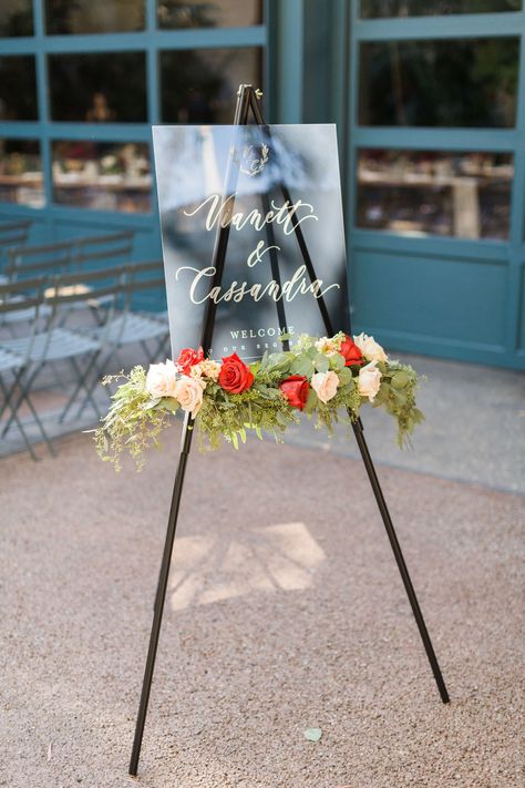 Modern Welcome Sign on Easel with Flowers and Elegant Calligraphy Easel Flower Arrangement, Easel With Flowers, Easel Sign With Flowers, Welcome Sign Flower Arrangement, Easel Decoration Ideas, Flowers On Easel Wedding Signs, Wedding Welcome Sign Floral Arrangement, Floral Easel Welcome Signs, Red Flower Arrangements