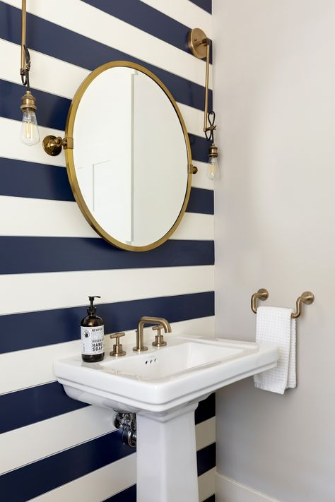 Statement wall with the gold fixtures and gold finished mirror gives off an elegant lakehouse feel. Love the simplicity combined with a fun pattern. Nautical Interior Design, Navy Bathroom, Nautical Interior, Blue Accent Walls, Nautical Bathroom Decor, Coastal House, Striped Walls, Powder Room Design, Nautical Bathrooms