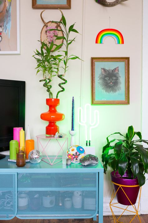 The orange plant stand and pink pedestal are both made by Eric Trine and the blue TV stand is from IKEA. Tv Stand Maximalist, Tv Stand Decor Colorful, Wavy Tv Stand, Tv Stand Colorful, Orange Tv Stand, Colored Tv Stand, Colorful Tv Stand, Pink Tv Stand, Cute Tv Stand