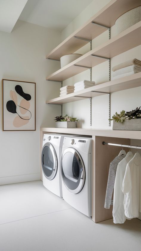 Stylish laundry room with minimalist shelving, white washer and dryer, indoor plants in concrete planters, and an abstract art piece on the wall.