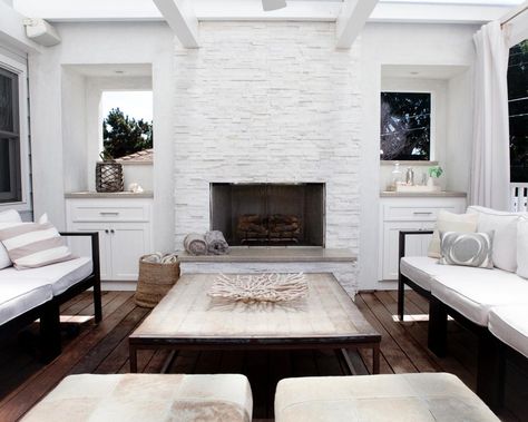 A white painted stone fireplace serves as the focal point of this modern coastal style deck. White curtains offer privacy or protection from the sun. A rectangular coffee table with a black frame mimics the black framed outdoor couches. Ledger Stone Fireplace, Stone Fireplace Remodel, Modern Stone Fireplace, Painted Stone Fireplace, White Stone Fireplaces, Stone Fireplace Designs, Stone Fireplace Wall, Ledger Stone, Stone Backsplash Kitchen