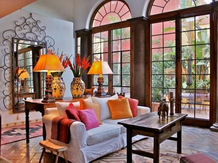 From the terra-cotta tile flooring to the tall arched French doors, this living room is a contemporary twist on traditional Spanish design. The warm accent colors look crisp against the white walls and sofa. The living room's color scheme is carried through to the adjacent traditional Spanish-style courtyard. Design by Carole Meyer Contemporary Mexican Interior Design, Spanish Style Living Room, Mexican Living Room, Spanish Living Room, Style Hacienda, Modern Mexican Home Decor, Spanish Interior Design, French Style Living Room, Modern Mexican Home