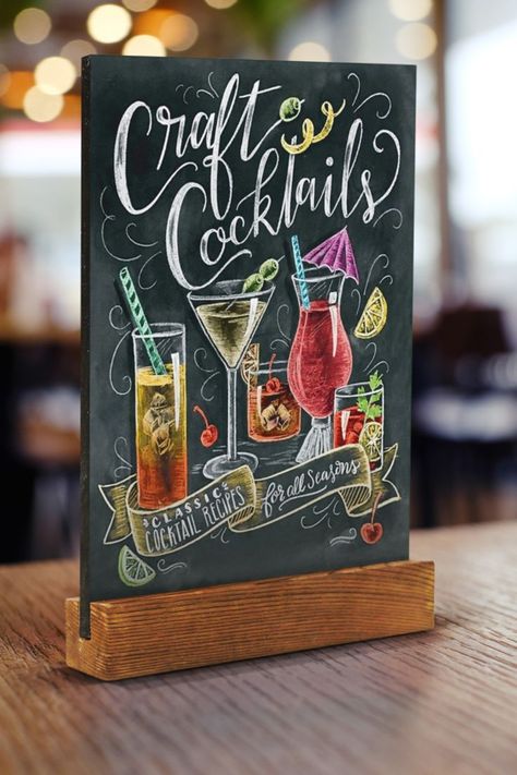 Chalkboard menu holder with wooden base on a tabletop and warm restaurant lighting in the background. The chalkboard features a cocktail menu drawn with chalk. Bar Chalkboard Ideas, Chalkboard Restaurant, Chalkboard Bar, Cafe Chalkboard, Chalk Menu, Menu Chalkboard, Starbucks Art, Cafe Display, Small Chalkboard