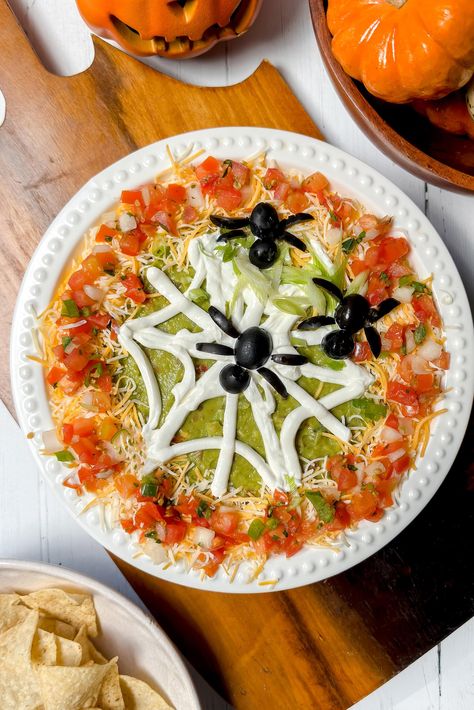 This Halloween 7 Layer Dip is a fun, delicious, and even spooky treat for kids and adults alike. A classic and easy party appetizer that's ready in 10 minutes, and can even be made ahead. Easy to make? Absolutely, including the edible spiders and their web! Spider Web Seven Layer Dip, Spooky Seven Layer Dip, Halloween Seven Layer Dip Spider Webs, Halloween 7 Layer Taco Dip, Spooky Halloween 7 Layer Dip, Halloween 7 Layer Dip, Edible Spiders, Halloween Food Snacks, Halloween Dip