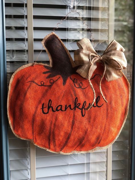 This pumpkin-shaped stuffed burlap door hanger is hand painted and reversible! Two door hangers in one! One side features a jack-o-lantern with smiling face, and the other side has a simple "thankful" in scripted letters. This hanger will include a removable bow and zip ties to attach it in your preferred location.  Measures approximately 21" across and is very lightweight and hangs quietly against a door. For indoor or covered outdoor use. This is a handmade, hand painted item made to order. Mi Burlap Pumpkin Door Hanger, Door Hangers Painted, Thanksgiving Door Hanger, Art Fundraiser, Burlap Pumpkins, Burlap Door Hanger, Pumpkin Door Hanger, Burlap Door, Pumpkin Door