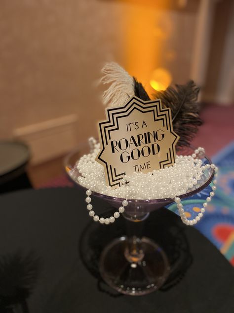 Giant Martini Glass Centerpiece for popular Roaring 20s party filled with beads, feathers & cute signage. #Roaring20sdecor #roaring20scenterpieces Roaring 20s Centerpieces Diy, Roaring 60s Party, Roaring 20s Graduation Party, Gatsby Centerpiece Ideas Roaring 20s, Gatsby Party Centerpieces Diy, Roaring 20s Diy Decorations, Roaring 20s Nye Party, End Of My Roaring 20s Party, Roaring 20s Party Centerpieces