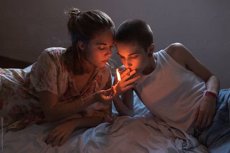 Two young women lighting a cigarette with a match while lying relaxed in bed. The light of the match illuminates their faces. Lighting Ciggerate Reference, Sharing Ciggerate, Lying In Bed Reference, Lighting Ciggerate Pose, Lighting Ciggerate, Two People In Bed, Lying On Bed Pose, In Bed Reference, Bed Reference