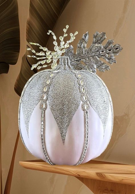 Introducing a new version of our glam pumpkin line! Celebrate the elegance of the fall and winter season with our exquisite white and silver pumpkin decorations. These glamorous accents are adorned with shimmering silver glitter and faux jewels, adding a touch of enchantment to any display. The featured item is a 13" pumpkin adorned with jewel spray, faux pear, and baguette-shaped crystals. When you make a purchase, you will receive one extra-large 13-inch x 11-inch silver and white pumpkin with Bejeweled Pumpkins, Glam Fall Decor, Christmas Pumpkins, Silver Pumpkins, Elegant Pumpkins, Painting Pumpkins, Pumpkin Decorations, Shaped Crystals, Silver Falls