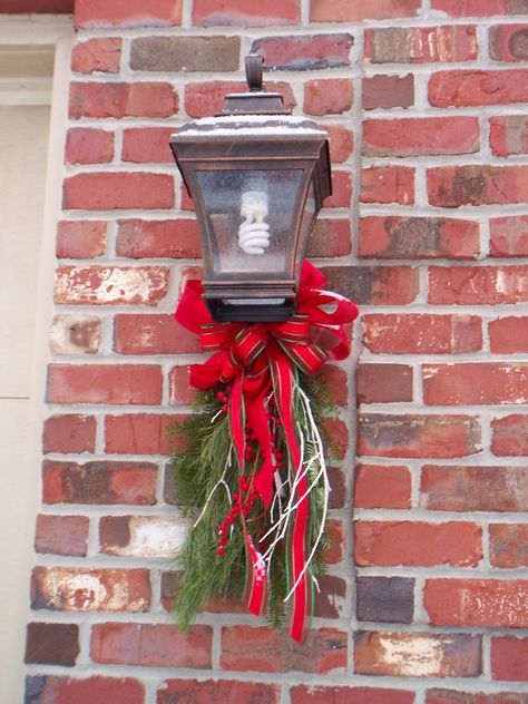 A simple holiday swag of fresh greens and pretty ribbon draw attention to the garage coach lights. Exterior Christmas Decorations, Outside Christmas Decorations, Wreath Hanging, Christmas Planters, Front Porch Christmas Decor Ideas, Porch Christmas Decor Ideas, Porch Christmas Decor, Christmas Decor Ideas Diy, Front Porch Christmas